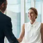 A photo of a man and woman smiling, shaking hands.