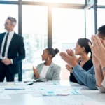 A photo of a group of people in a meeting clapping.